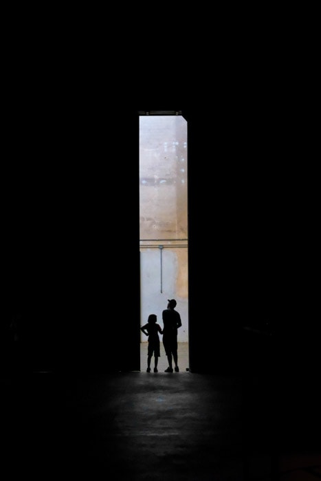 An essay photo of the silhouettes of a man and child standing in a dark doorway. 