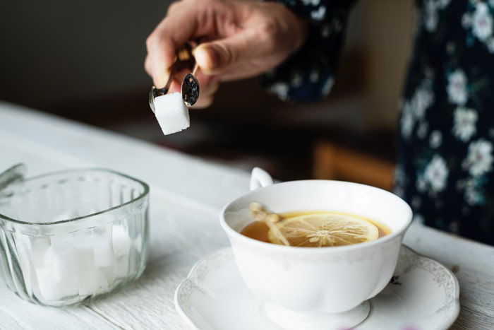  Photo essay detail of someone placing a sugar cube into a cup of tea.