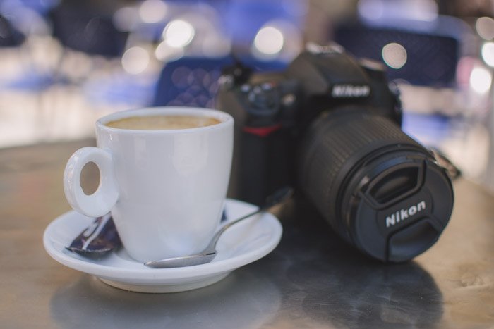Blurry photo of a Nikon camera and white coffee cup resting on a table - enjoy your time on your photo walk!