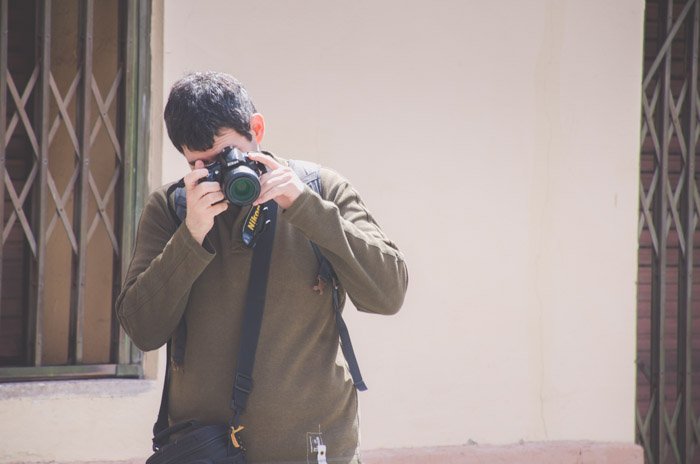 Photo of a man in dark green jumper taking a photo with a Nikon SLR camera during a photo walk
