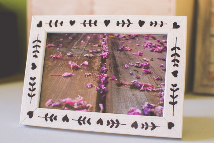 A photograph of pink flowers in a wooden frame decorated with a pattern of hearts and leaves made with black permanent marker as an idea for what to do with photos