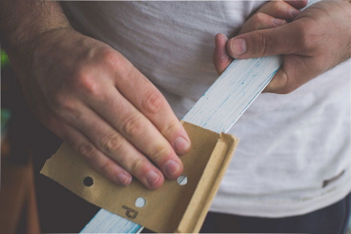 A close-up of a hand sanding a wooden board to hang pictures on as an idea for what to do with photos