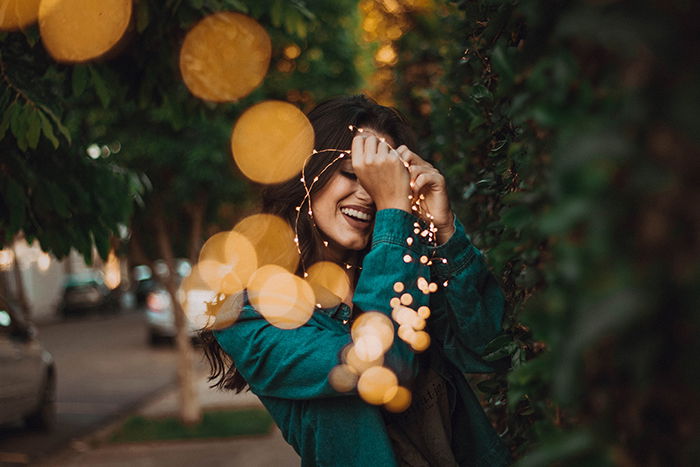 Dreamy portrait of a girl holding fairy lights beside bushes. Self portrait photography tips.