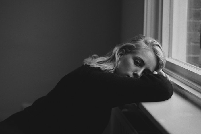 Black and white portrait of a blond girl leaning on a window sill. Self portrait photography tips.