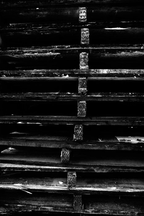 A shadowy black and white photograph of a stack of wooden palettes.