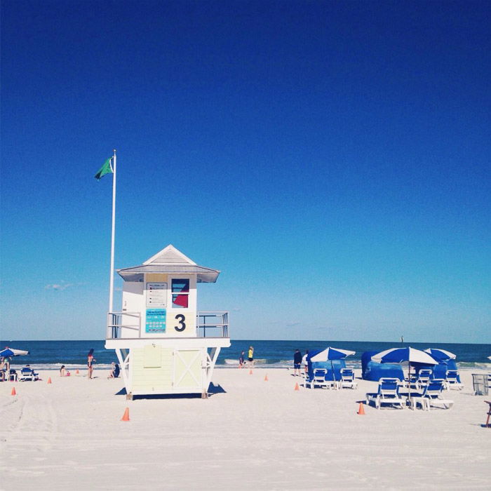 A photography of the beach with lifeguard hut and beach chairs. 