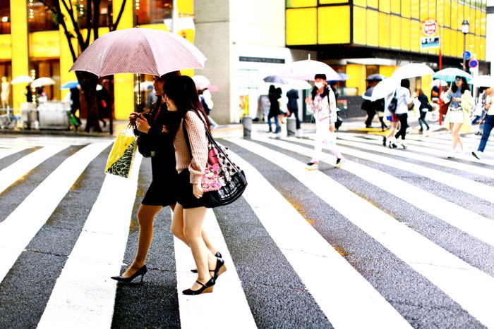 Travel photography of two women with umbrellas crossing the street, busy street scene background.