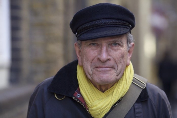 Street photography portrait of a man in a dark peaked capped and yellow scarf, looking at the camera