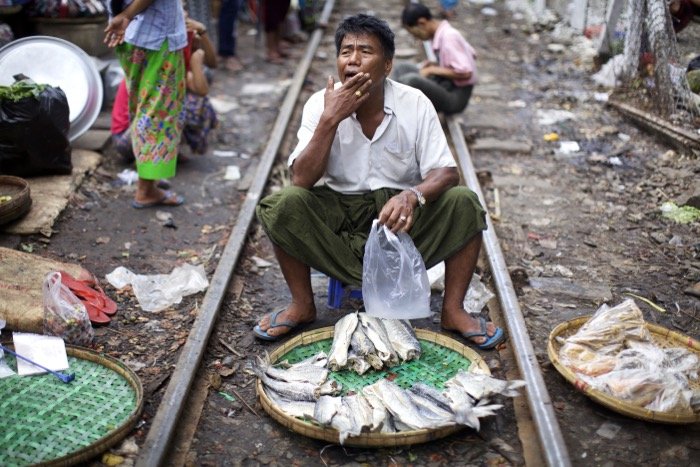 fish market scene, a man sits between train tracks with a basket of fish in front of him. street photography