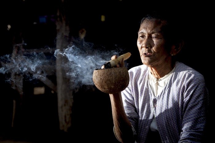 Street photograph of an old woman smoking a large cigar and using a coconut shell as an ashtray