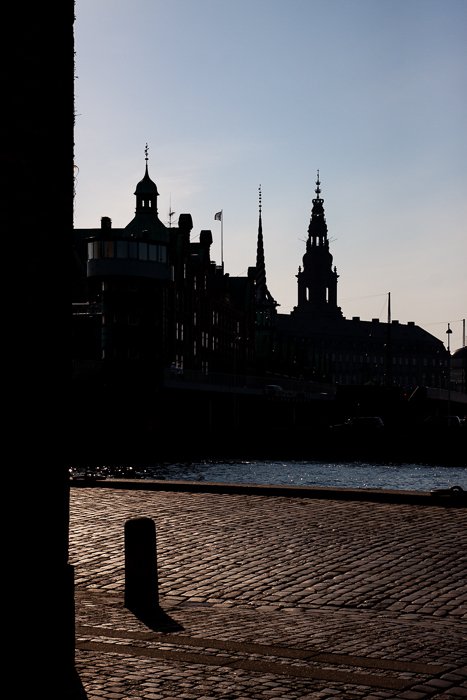 silhouettes of city buildings against the bright sky, in the background of shadowy street and river in Copenhagen 