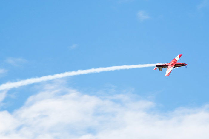 An airshow photography shot of a red airplane flying with a stream of contrails behind