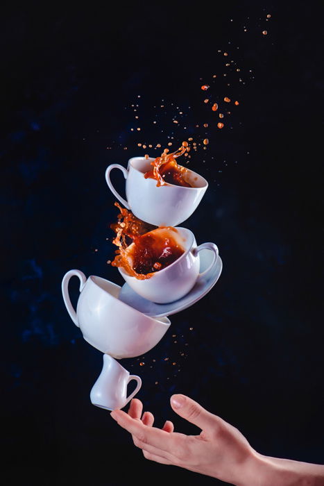 A still life photography shot of balancing cups with coffee splashes on dark background - creative photography ideas