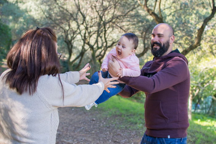 Family portrait photo of a couple playfully passing their baby 