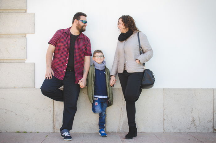 Family portrait photo of a couple and son leaning against a wall