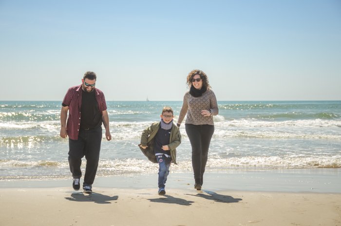 一对夫妇和儿子在海滩上散步的全家福照片