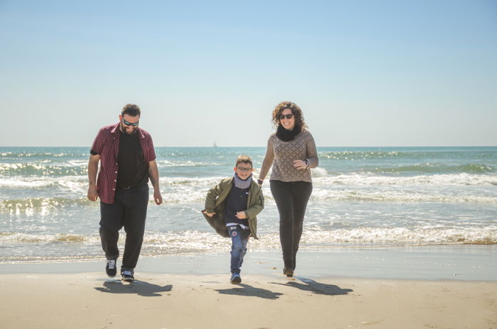 Family portrait photo of a couple and son walking on a beach