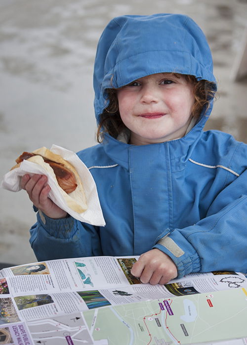 Portrait photography of a little girl in a blue rain jacket holding a sausage roll. Street photography tips