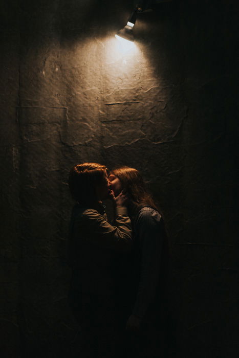 A couple kissing in front of a textured wall with a single light source