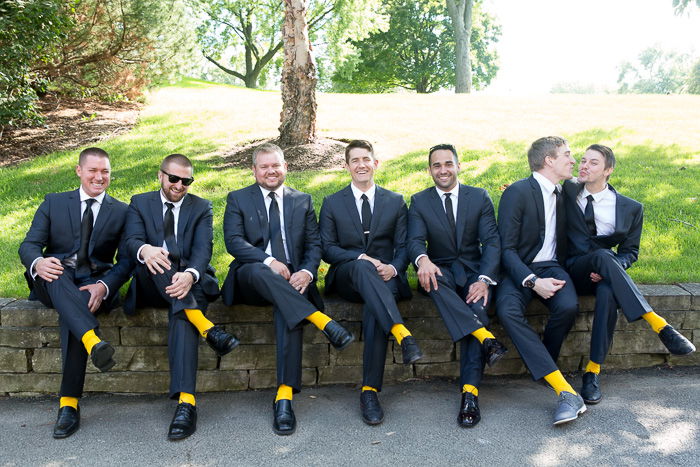 Humorous wedding photo of seven groomsmen sitting on a wall, all wearing yellow socks