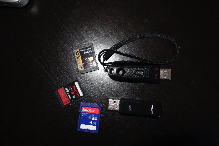 Overhead shot of USB thumb drives and SD cards for travel photography best way to backup photos on black table