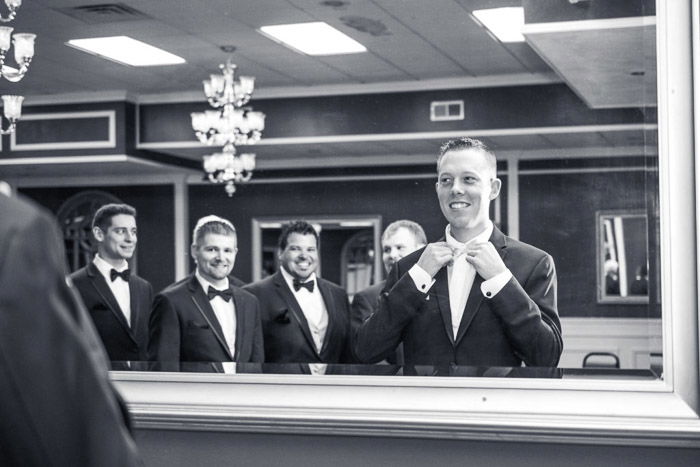 Black and white wedding photography a groom straightening his collar in a mirror