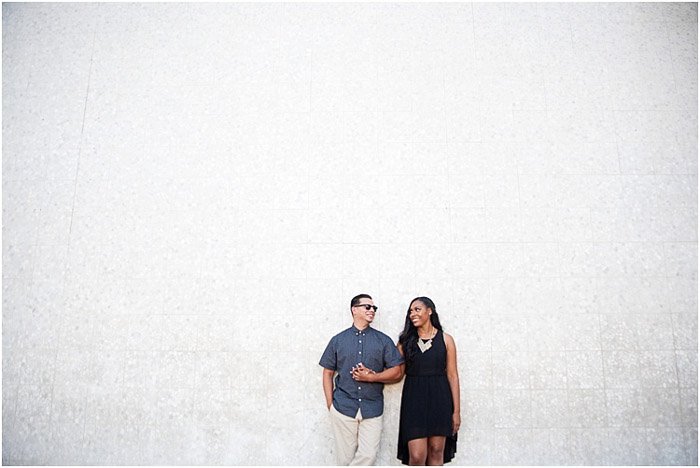 An engagement photography photo of a couple standing against a spacious white wall