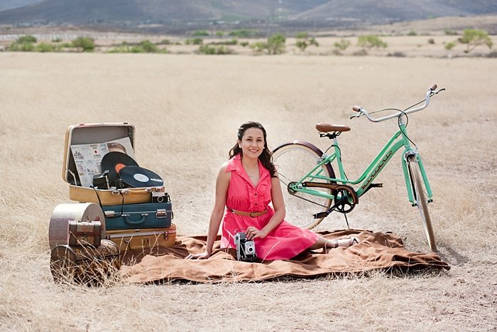 A girl in pink dress posing outdoors on a rug with bicycle and suitcases - environmental portrait lighting tips 