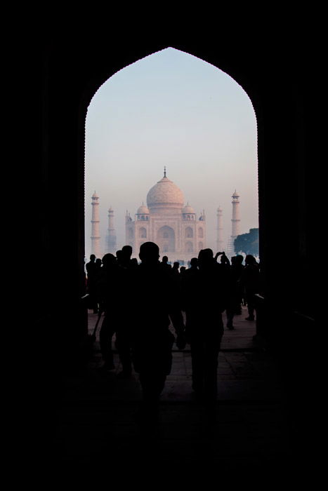 Photo of the silhouettes of people walking through an archway which is naturally framing the photo. 