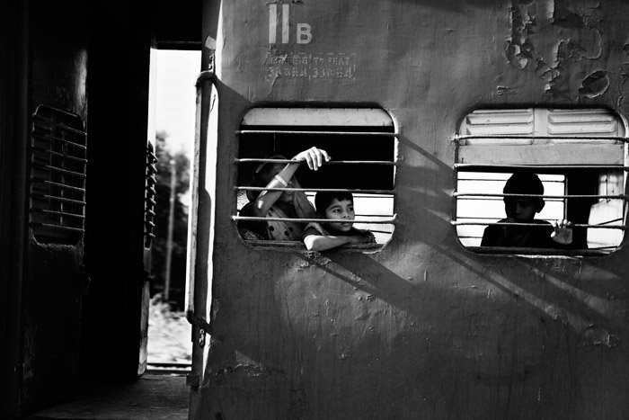 Black and white documentary photograph of boys looking out from a train window. Naturally framing photography.