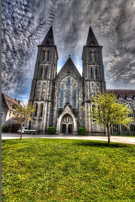 An over processed HDR photograph of Maredsous Abbey with black clouds, halos, and overcooked looks.