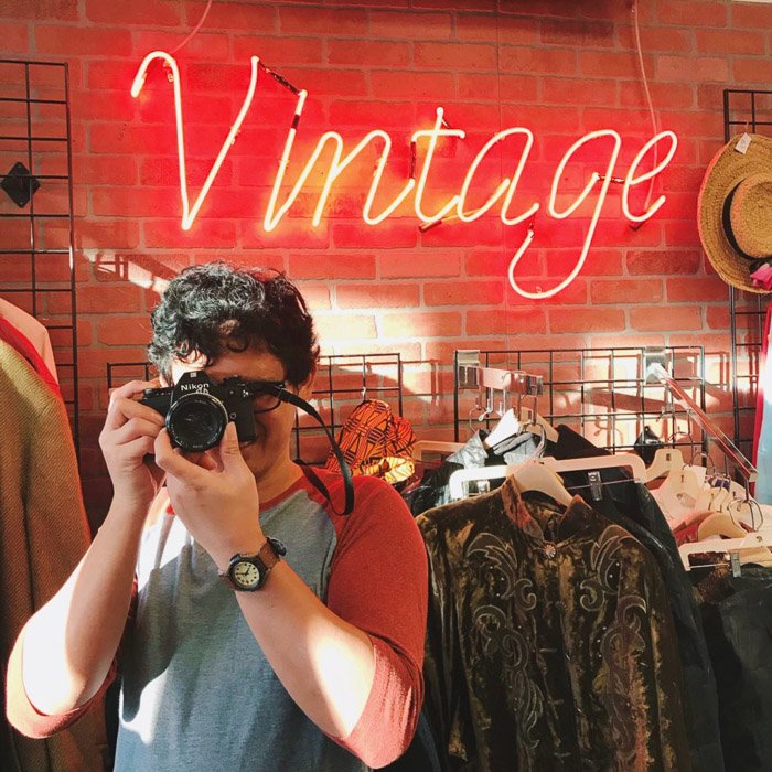 Portrait photography of a man in a vintage clothes shop holding a camera. Instagram tips for social media photography.