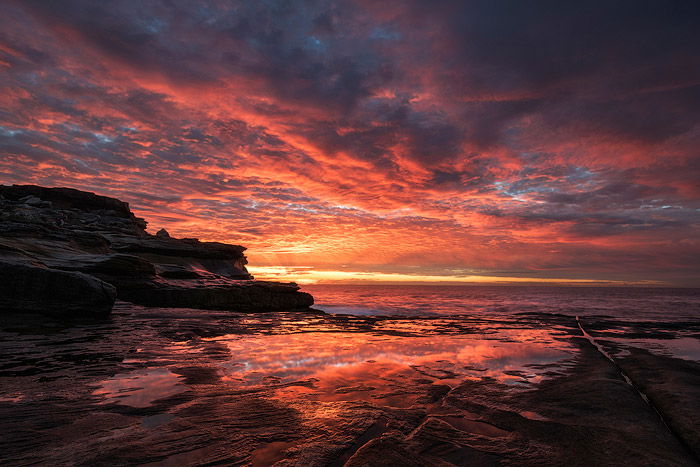 Rocky seascape photo shoot with dramatic pink clouds reflected on the water below.