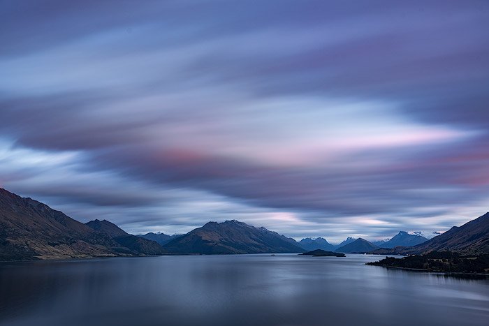 Long exposure landscape photo shoot showing fast moving clouds over mountains and water.