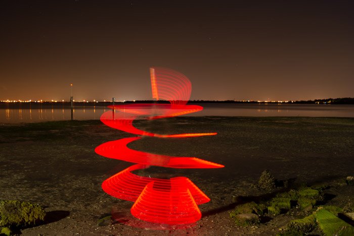 A red light paighting photography spiral on a beach at night.
