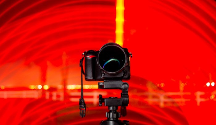 A DSLR camera on a tripod surrounded by a red light spiral.