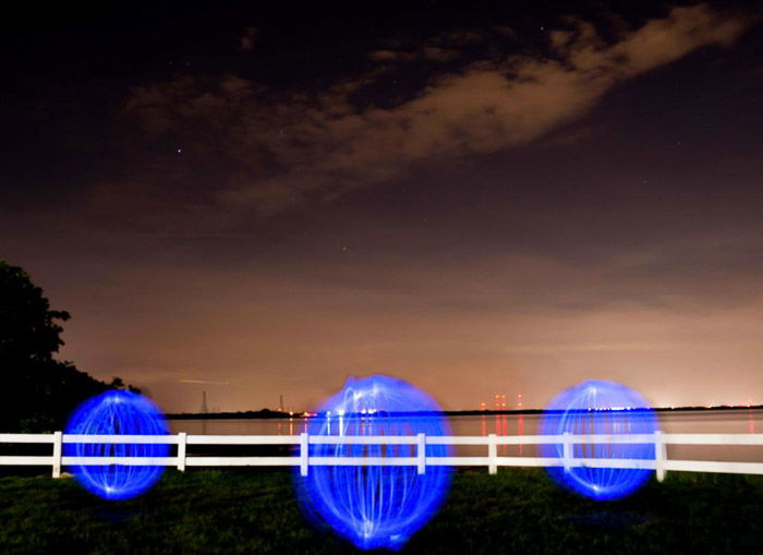 Three blue light painting orbs on a beach at night.