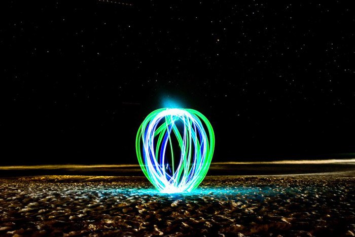 A green and blue light painting orb on a beach at night.