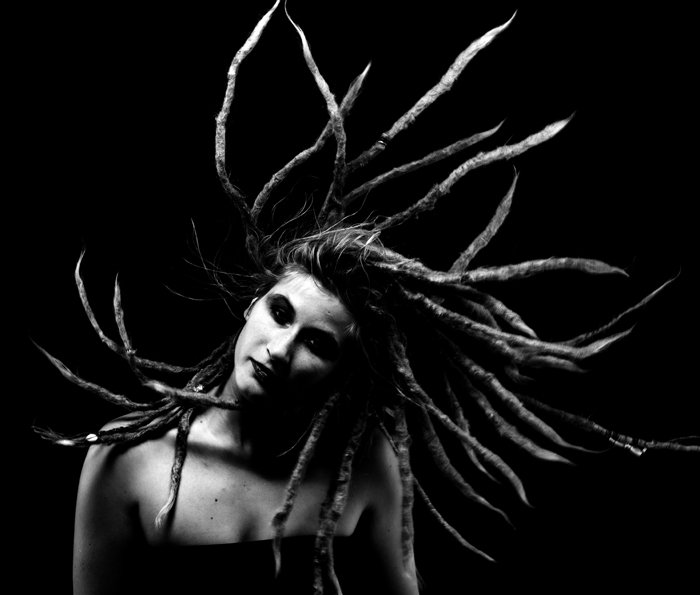 A low key monochrome photography portrait of a girl with dreadlocks, swinging her hair.