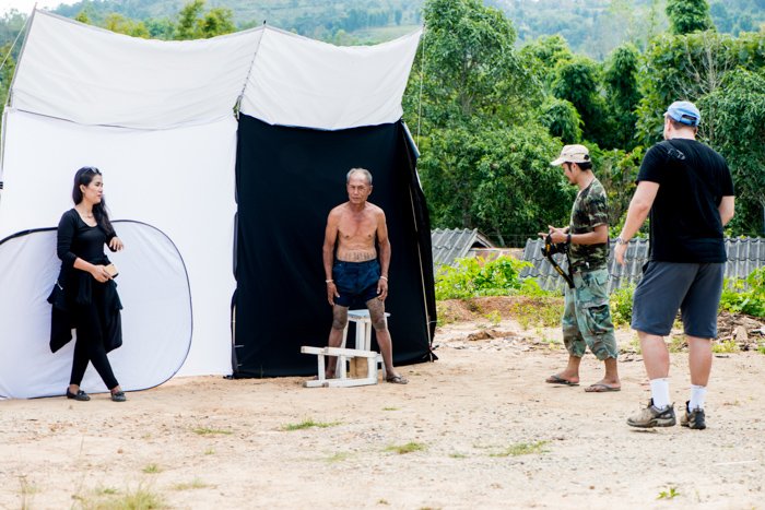 An outdoor portrait photography studio set up in a village showing the diffuser above, the bare earth used as a reflector in front and the large fold out reflector.