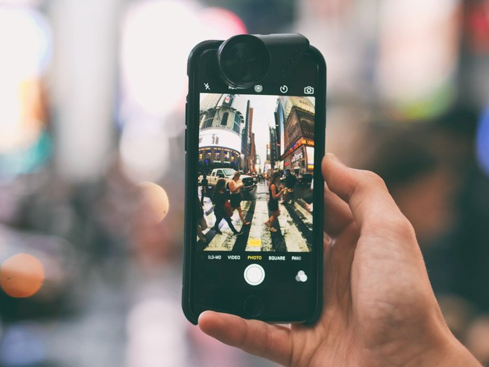 A hand holding a smartphone to take a photo of a busy street scene