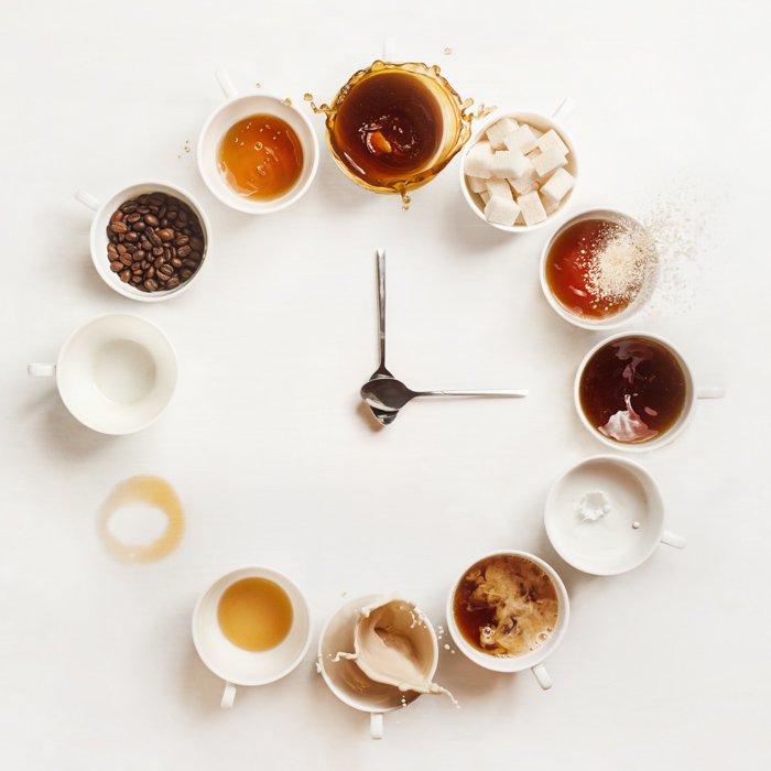 Still life photo of a "clock" made up of teaspoons and coffee cups filled with coffee, beans, and sugar