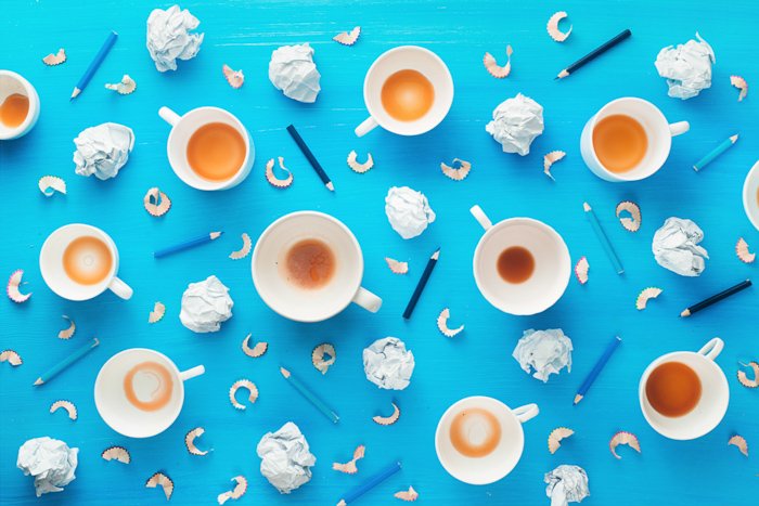 Creative overhead still life photography idea of cups with some coffee, crumpled paper balls and pencil shavings on a colorful blue background