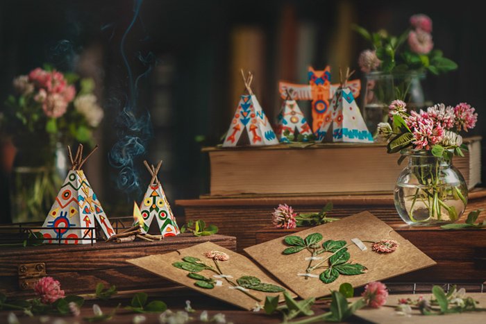 Tiny teepees, with books, flowers, and leaves arranged on a table to create a miniature still life scene