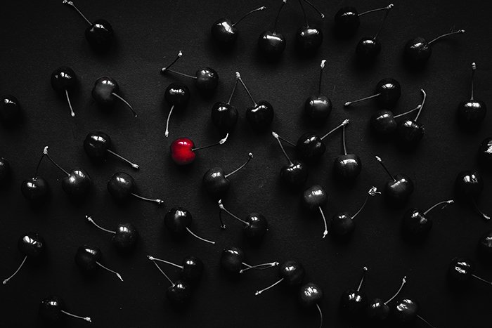 Elijah O'Donell overhead surreal photography of black cherries, one red, on a black table