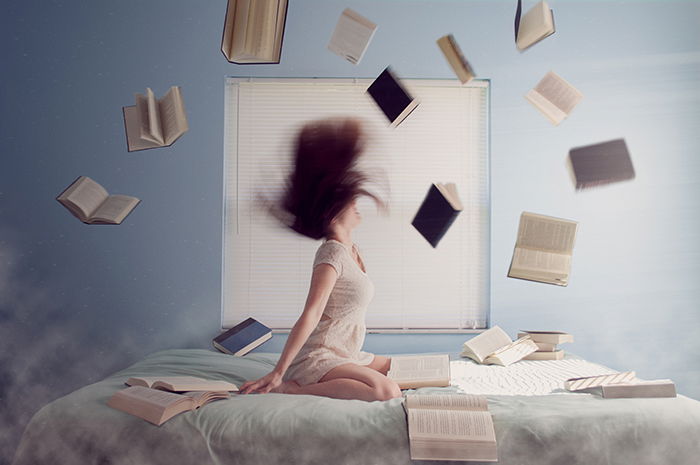 Laci Slezak surrealism photography of a girl sitting on a bed, books flying around.