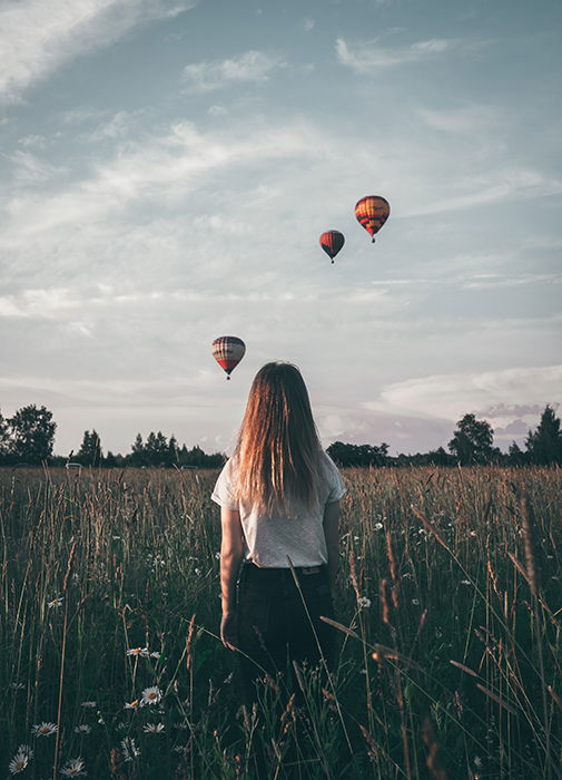 Natalya Letunova artistic photo of a girl standing in a field watching hot air balloons in the sky - surreal photography