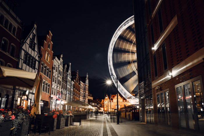 A street scene at night with a moving ferris wheel captured with a time-lapse camera