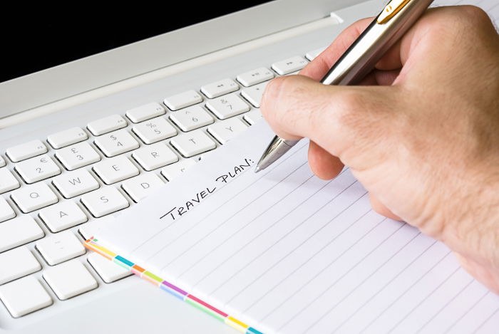 Photo of a hand writing a travel plan in a notebook, preparing a travel photography shot list