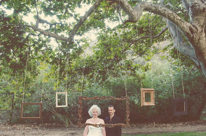 A cool wedding photo booth set up outdoors with various sized photo frames hanging from a large tree branch